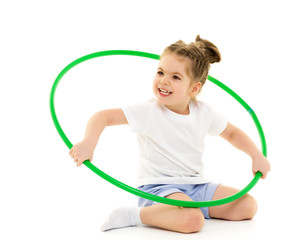 A little girl in a white T-shirt performs exercises with a hoop.