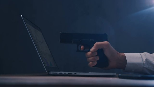 Male hand aims the gun at the computer screen. Concept of cyber robbery.