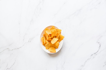 Nacho chips in white bowl lying on marble background . Unhealthy food concept. Flat lay, top view, overhead, copy space, place for text