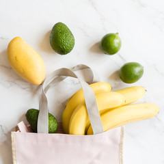 Top view pink bag of different fresh health food lying on white marble background. Overhead. Flat lay. Minimal reusable waste concept