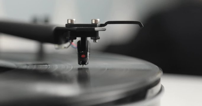 Needle and arm on spinning vinyl record turntable player, closeup side view at blur background.