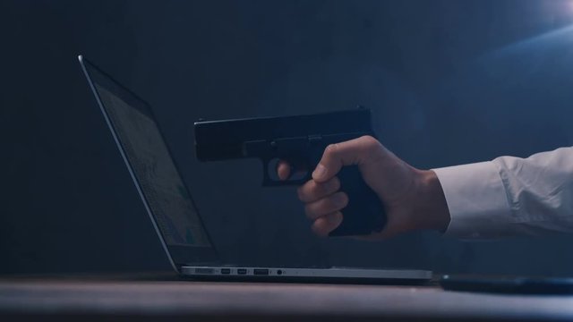 Arm with gun aims at a screen of laptop. Cyber robbery.