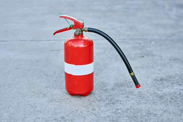 A single isolated fire extinguisher on concrete in safety red with a white tape strip around the middle.