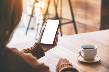 Mockup image of a woman holding black mobile phone with blank desktop screen with coffee cup on the table