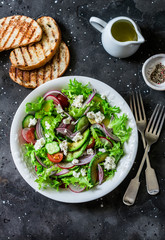Vegetarian avocado, vegetables, feta cheese salad and grilled bread - delicious healthy lunch, snack on a dark background, top view