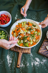 Family vegan lunch or vegetarian dinner. Mother hands put vegetables on dish, gives food to child, kid. Healthy food. Top above view on table.