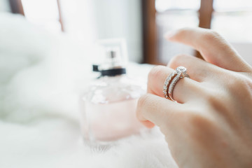 Close up of diamond rings on woman finger with blurry white wool and perfume background. Love and...