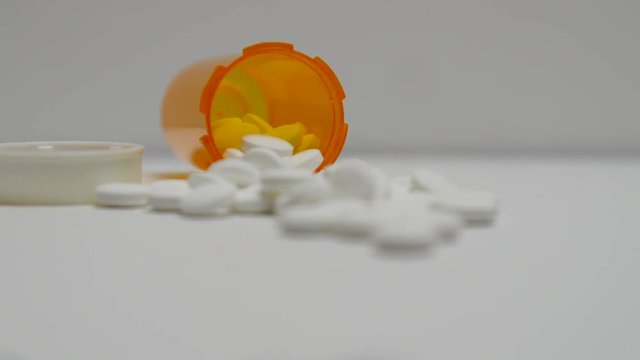 Pills spill out of bottle on white surface.