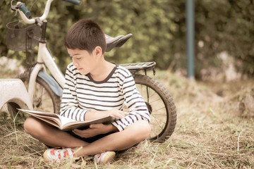 Little boy reading book sitting with bicycle in the park