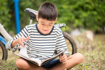 Little boy reading book sitting with bicycle in the park