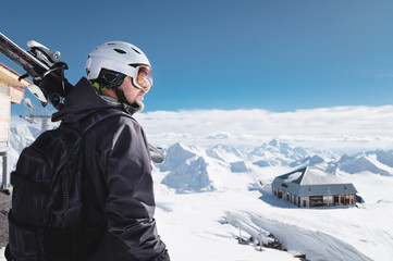 Close-up Portrait bearded male skier aged against background of mountains. An adult man wearing ski googles mask and helmet skis on his shoulder looks mountains. Ski resort concept