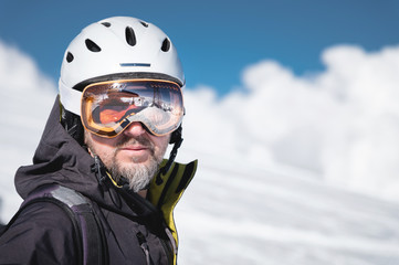 Close-up athlete skier in helmet and ski mask against the snow-capped mountains of a ski resort with a reflection of the Caucasian mountains in the mask