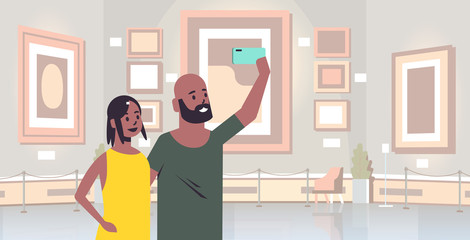 young couple taking selfie photo on smartphone camera african american man woman visitors in modern art gallery museum interior portrait horizontal