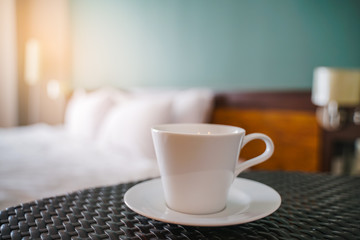 cup of coffee ,in soft focus , on table with blurred bed and morning light