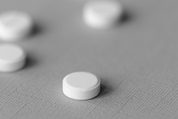 White tablets scattered on a gray surface close up. Black and white