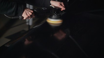 Car detailing - Hands with orbital polisher in auto repair shop. Selective focus. Car polishing and LCP correction