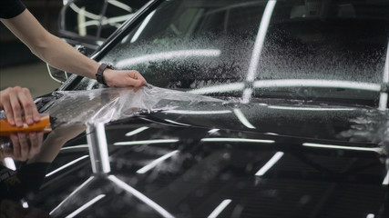 professional applying protective film to the red car. Master glues a protective film on the hood of...