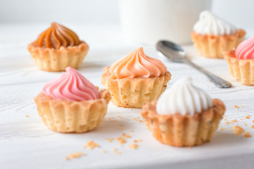 Small cakes and with cream on a white table with a spoon and a mug. Selective focus. 
