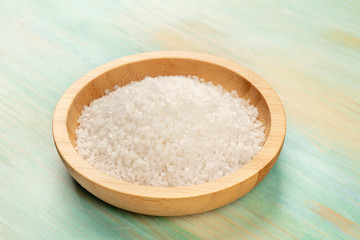 A closeup photo of a bowl of sea salt on a teal blue background