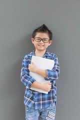 Asian boy feels happiness when time to school and his hands hold the book against the gray wall