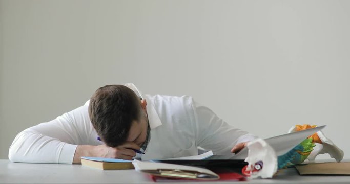 Portrait of young tired doctor roentgenologist falls asleep doing paperwork in his workplace at white background, front view.