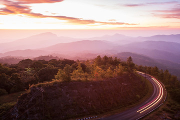 Beautiful mountain road at sunrise, curve asphalt road with light trail from headlights leading through mountain range. Doi Inthanon, Chiang Mai, Thailand. © Tanes