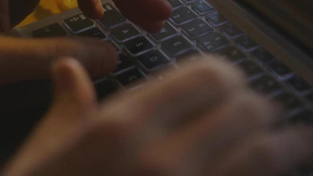 Handheld, interior, medium close up shot of hands typing on a computer keyboard.