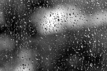 Raindrops on glass in rainy weather close up. Natural background black and white