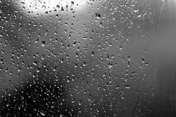 Raindrops on glass in rainy weather close up. Natural background black and white