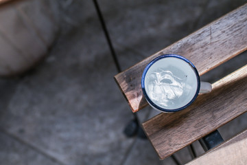 A white cup of ice water on wooden chair 