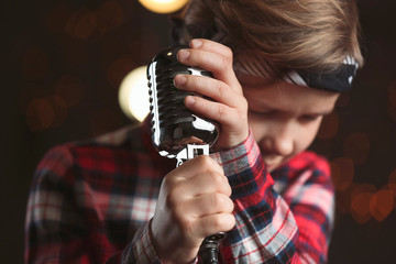 Cute little boy with microphone on dark background, closeup