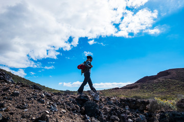 Hiking people on the outdoor nature mountains with lady and backpack walking in leisure activity - blue sky and green valley landscape with lady doing trekking alone