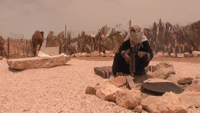 Bedouin woman by campfire baking traditional bread in oasis on Negev Desert