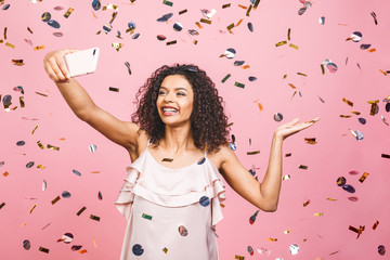 Portrait of a smiling young african woman taking selfie with mobile phone over pink background with...