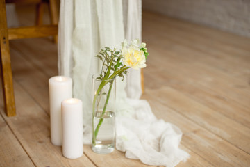 Obraz na płótnie Canvas Branch of blooming white peony tulip Mattiola branch in a glass vase white wax candles stand on the wooden light floor indoors