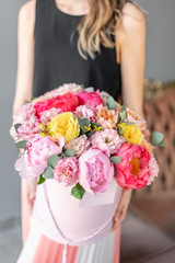Obraz na płótnie Canvas coral and pink peony. Beautiful bouquets of mixed flowers in womans hands. Packed in a round box of hat. Floral shop concept . Fresh cut Flowers delivery