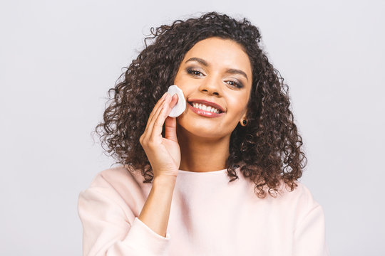 Smiling woman removing makeup. Photo of african american woman holds cotton pads near face isolated on white background. Skin care and beauty concept.