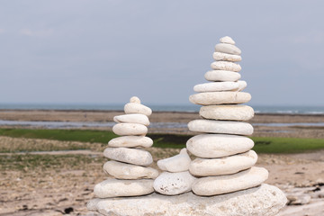 Fototapeta na wymiar Pyramid of white grey stones on the sandy beach at ocean background