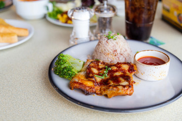 Chicken steak with rice and sauce in white dish.