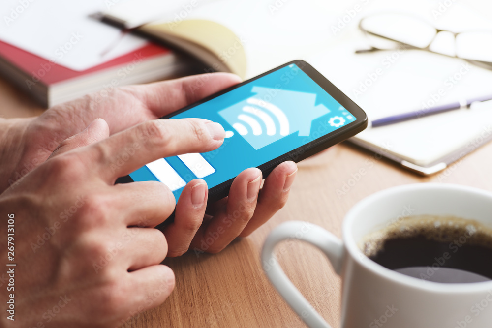 Poster Smart home and IOT concept.Closeup of male hands touching smartphone screen for using smart home app at table.