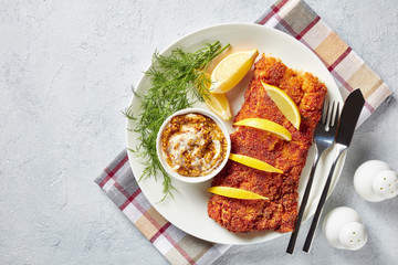Breaded hake fillet on a plate, top view