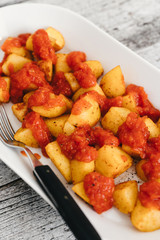 Patatas Bravas, oven-baked potato cubes traditionally served as tapas in Spain with spicy mojo rojo, a red hot salsa made of tomatoes, bell peppers, onions and chile on white plate  and wooden table