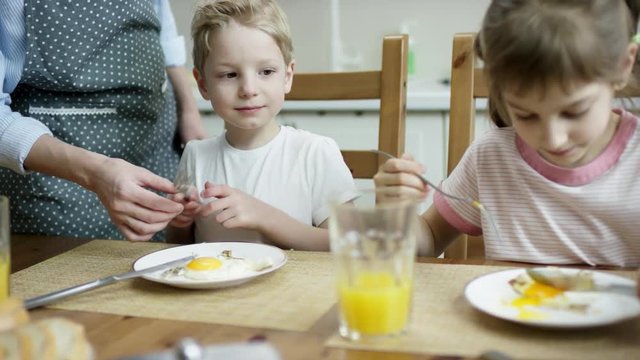 mother give a fork to her son to eat scrubled eggs during the family dinner