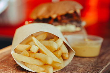 Delicious fresh homemade cheese burger with meat, cheese, tomatoes, lettuce and onion rings in Kraft paper and french fries . street food on wooden table  on wooden background