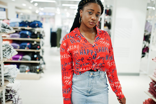 Modish African American Woman In  Red Shirt And Jeans Skirt Posed At Clothes Store. It's Time For Shopping.