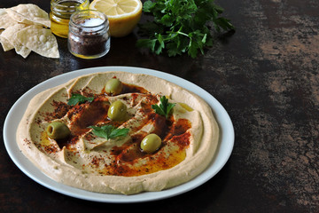 Fresh hummus with olives, paprika and parsley on a plate.