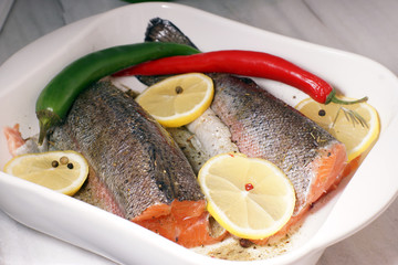Red trout fish, ready to be baked in the oven with lemon and hot pepper in a white heat-resistant dish