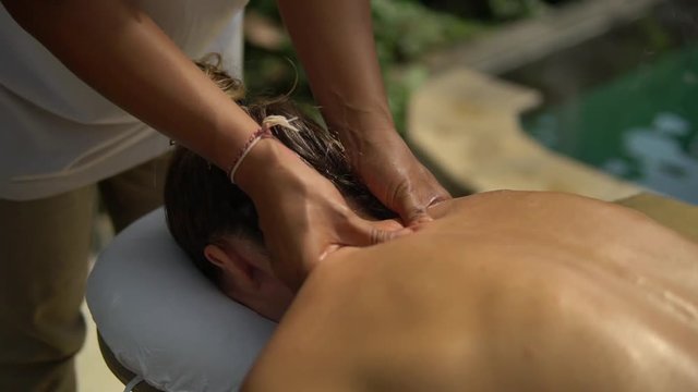 close-up Thai masseuse makes neck massage in spa outside area for young client