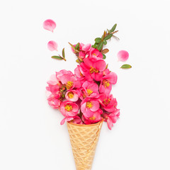 Waffle cone with bouquet of pink spring flowers on light background. Creative spring minimal concept. Flat lay top view copy space. Spring or summer mood concept