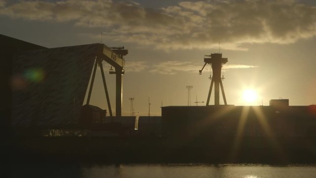 Steady, exterior, wide shot of large machinery and a building, shadowed by a bright sun.